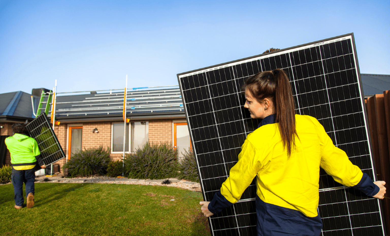A solar panel installer carrying solar panels towards a home