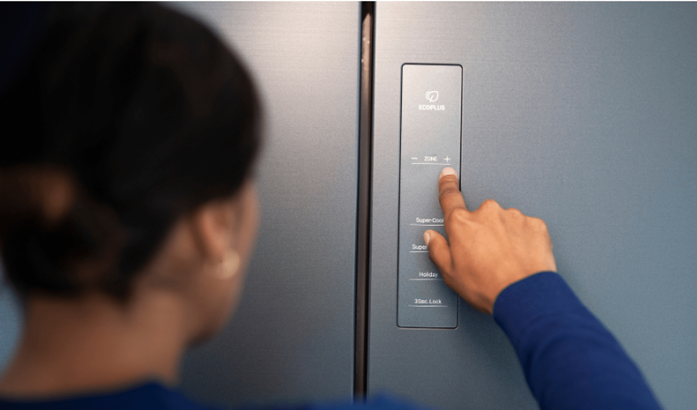 A person adjusts the temperature settings on a refrigerator using the external control panel in an all-electric home.