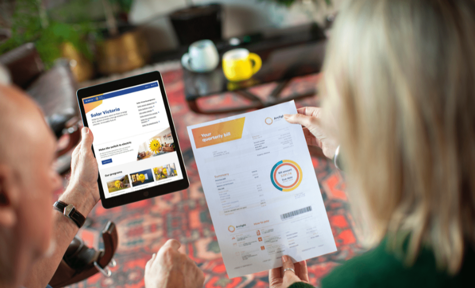 Two people review an energy bill and Solar Victoria information on a tablet while seated at a table in a home.