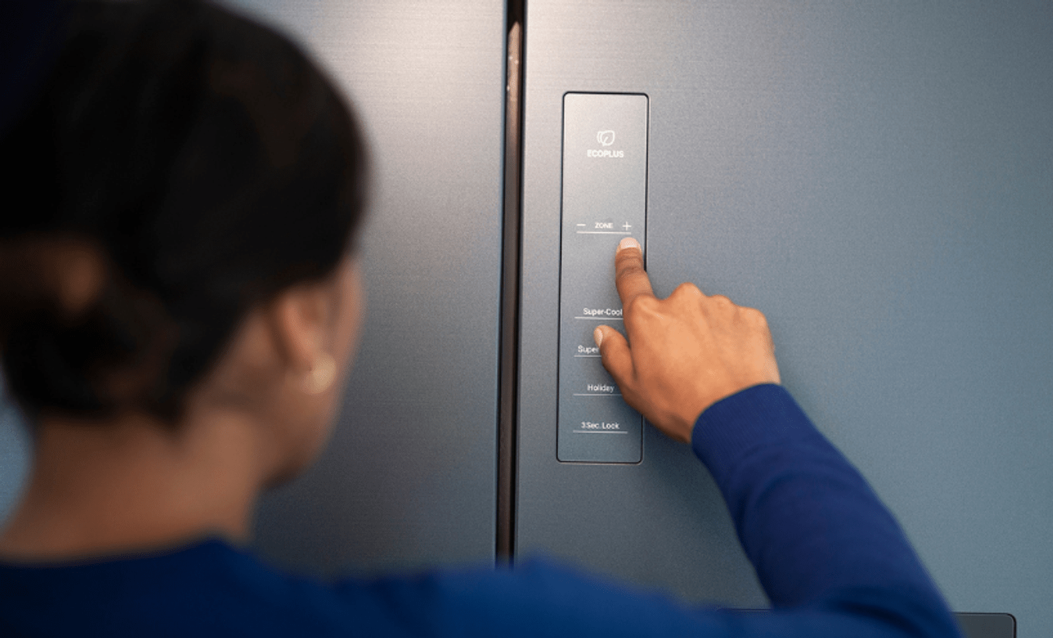 A person adjusts the temperature settings on a refrigerator using the external control panel in an all-electric home.