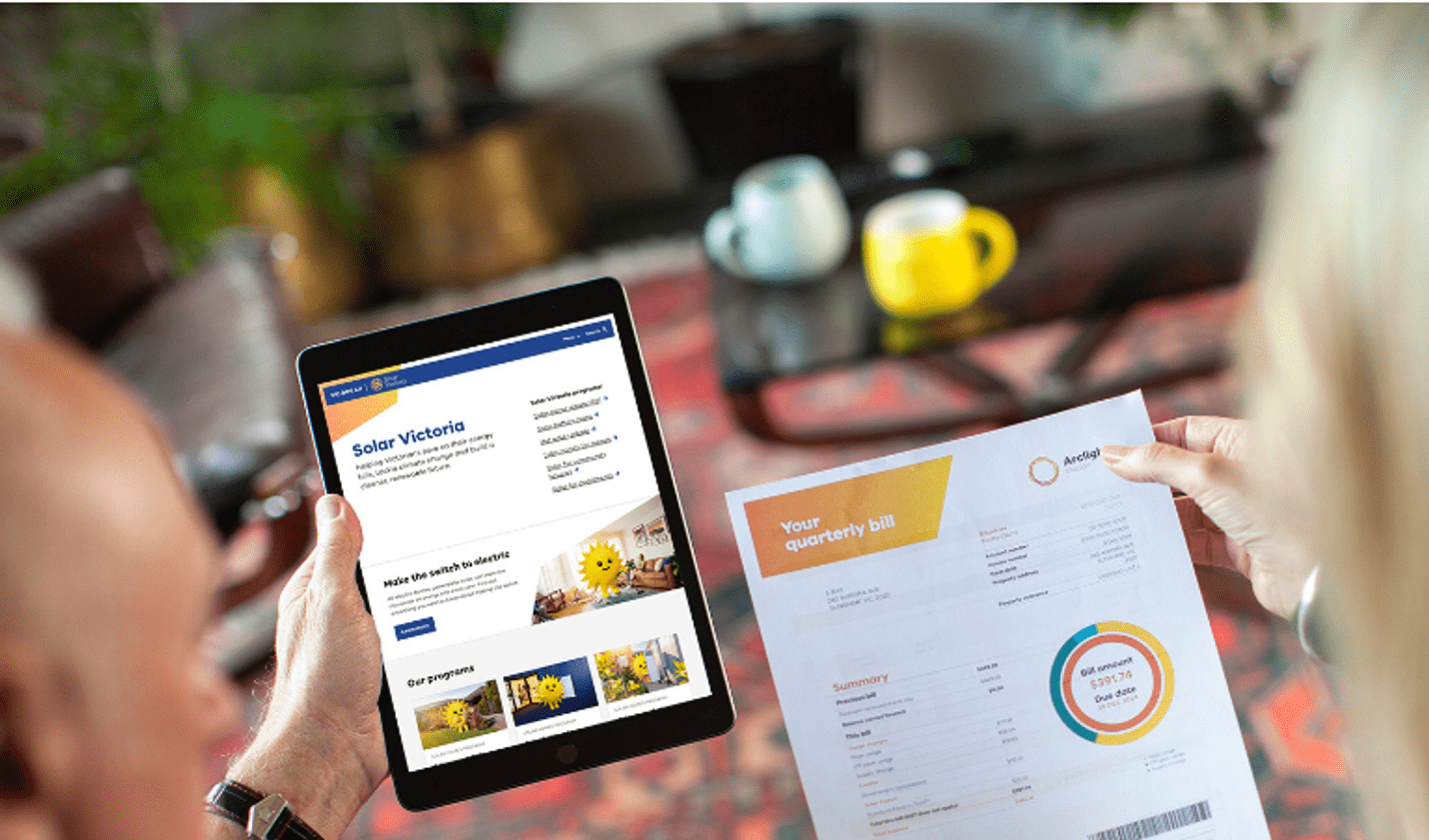 Two people review an energy bill and Solar Victoria information on a tablet while seated at a table in a home.